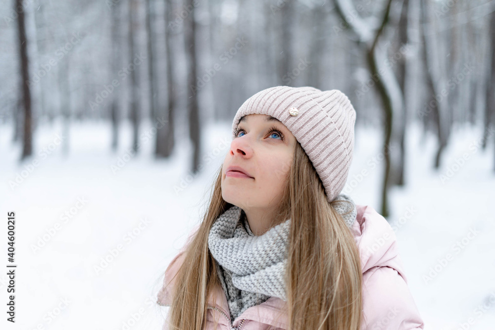 girl in the winter forest in a pink hat, gray scarf and pink jacket looks up girl in the winter forest in a pink hat, gray scarf and pink jacket looks up
