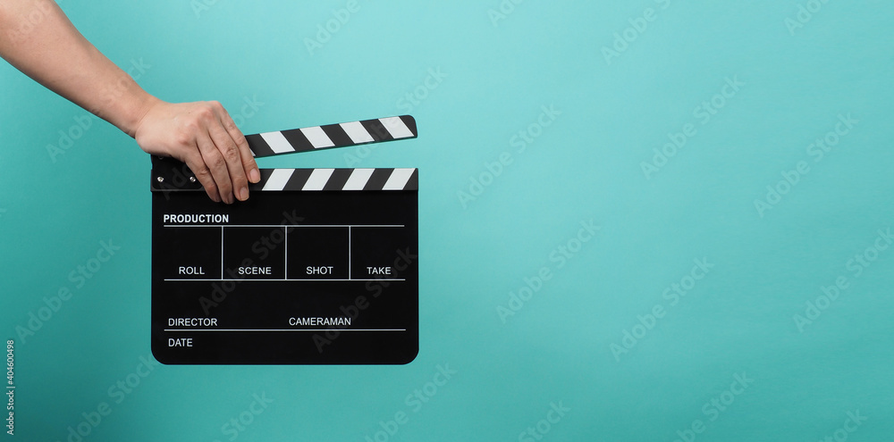 Hand is holding Black clapper board or clapperboard or movie slate on blue and green or Turquoise background.