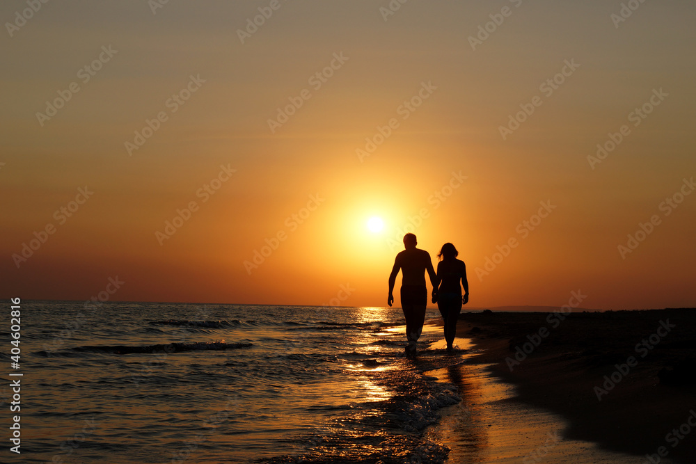 Silhouette Young romantic couple walks along the coast at sunset and hold hands