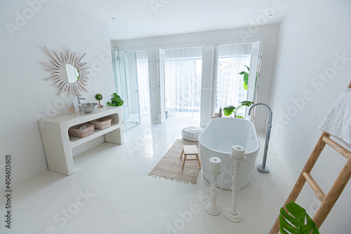 Extra white and very light minimalistic stylish elegant interior of bathroom with modern bath, green plants and wooden elements