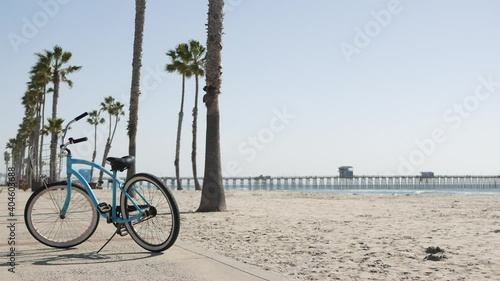 Blue bicycle, cruiser bike by sandy ocean beach, pacific coast near Oceanside pier, California USA. Summertime vacations, sea shore. Vintage cycle, tropical palm trees, lifeguard tower watchtower hut