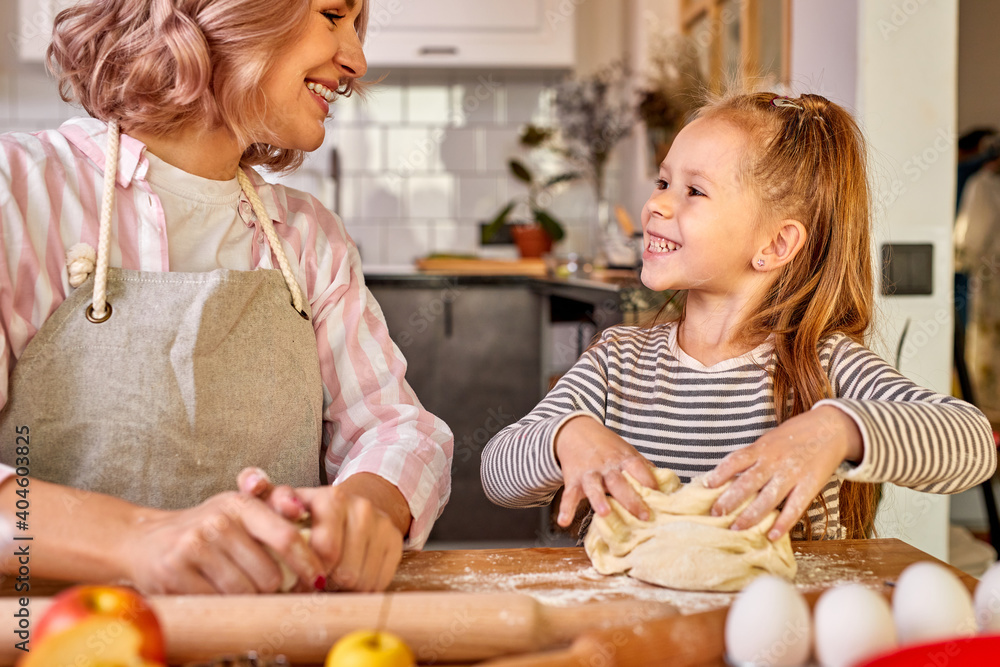 mother and pretty daughter cooking together, enjoy process and communication. woman teach her daughter kneading dough for domestic cookies mother and pretty daughter cooking together, enjoy process and communication. woman teach her daughter kneading dough for domestic cookies