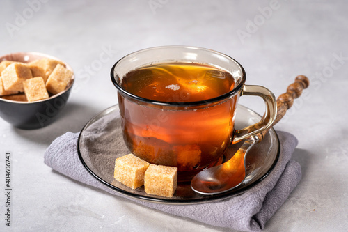 Glass cup of black tea with sugar cubes on light background