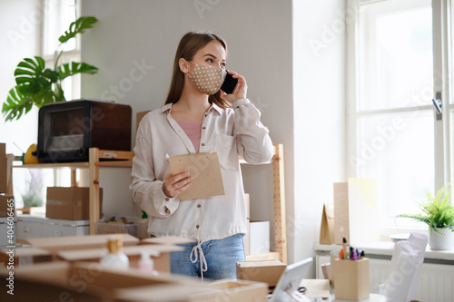 Young woman dropshipper with smartphone working at home, coronavirus concept. photo