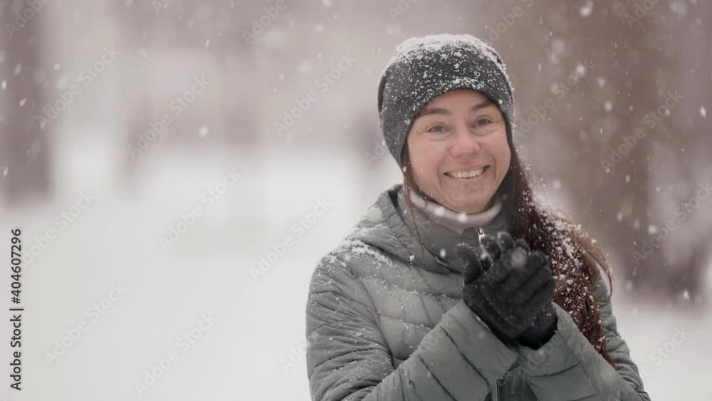 Close-up portrait of a dark-haired middle-aged woman, she is on the street on a winter day, posing smiling, catching snow with her hands. Snowy weather in the city park. Close-up portrait of a dark-haired middle-aged woman, she is on the street on a winter day, posing smiling, catching snow with her hands. Snowy weather in the city park.
