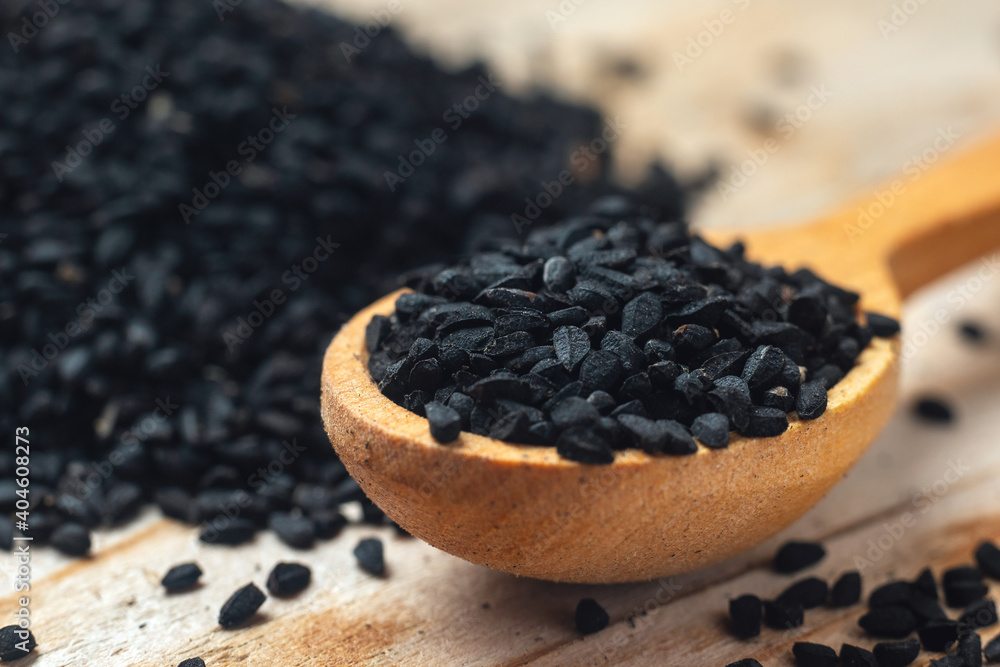 Black cumin seeds on wooden spoon on wooden background Black cumin seeds on wooden spoon on wooden background