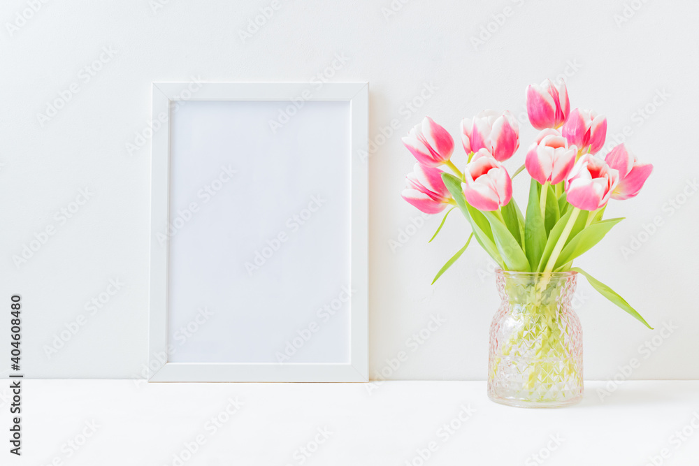 Home interior with decor elements. Mockup with a white frame and pink tulips in a vase on a light background Home interior with decor elements. Mockup with a white frame and pink tulips in a vase on a light background