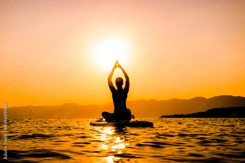 girl at sunset on a paddleboard is engaged in yoga. hands up at