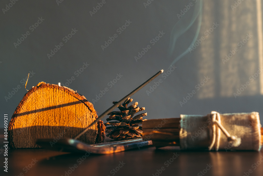 Burning incense stick in a scene natural and wooden decoration objects during sunset. Selective focus on stick tip ash. Cozy home environment. - obrazy, fototapety, plakaty 