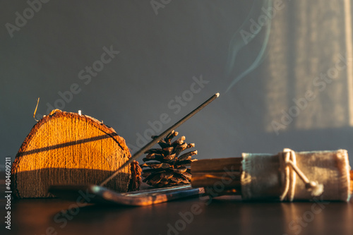 Burning incense stick in a scene natural and wooden decoration objects during sunset. Selective focus on stick tip ash. Cozy home environment. photo