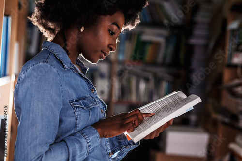 Young black female student reading a book in college library.	
 photo