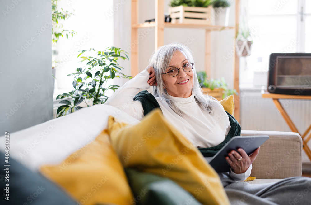 Portrait of senior woman sitting indoors on sofa at home, using tablet. Portrait of senior woman sitting indoors on sofa at home, using tablet.
