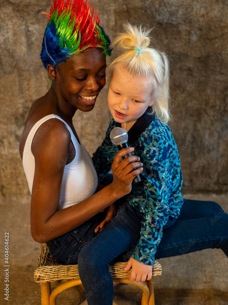 Φωτογραφία African American woman in white bodysuit and jeans in bright multicolored punk wig and white blond boy singing karaoke with microphone and fooling around