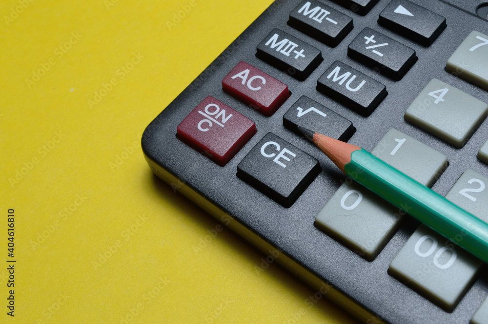 calculator and pencil lie on a yellow background. close-up. calculator and pencil lie on a yellow background. close-up.