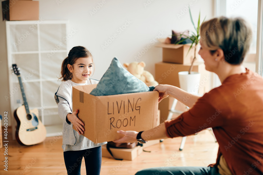 Φωτογραφία Happy little girl and her mother unpacking their belongings while moving into new home