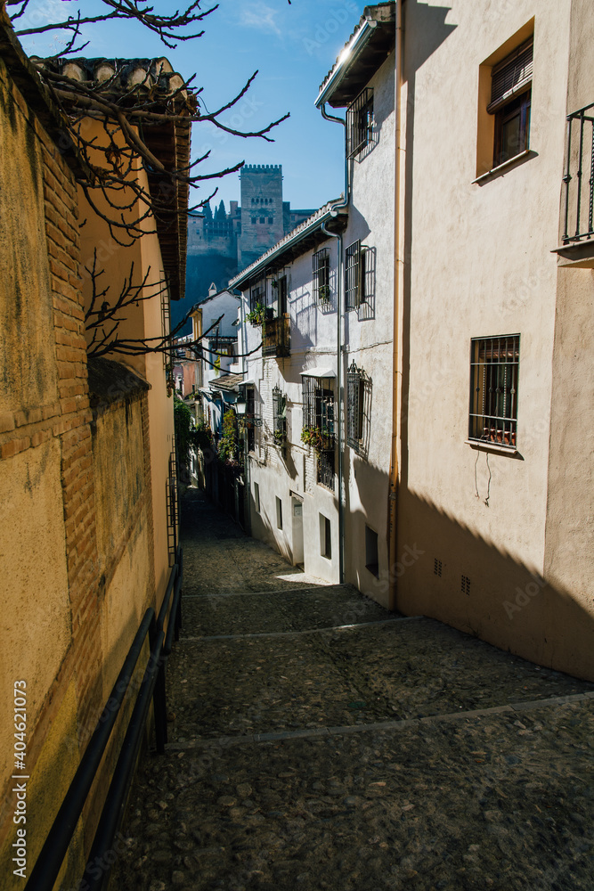 Jewish street in Granada, Spain, at noon with harsh light and Alhambra palace fortress in the back