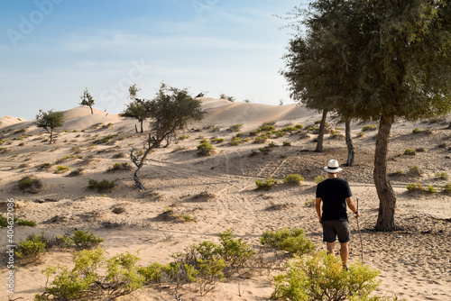 Back view of a man standing on the sand dunes next to some small trees and shrubs in Sharqiya Sands, Oman.