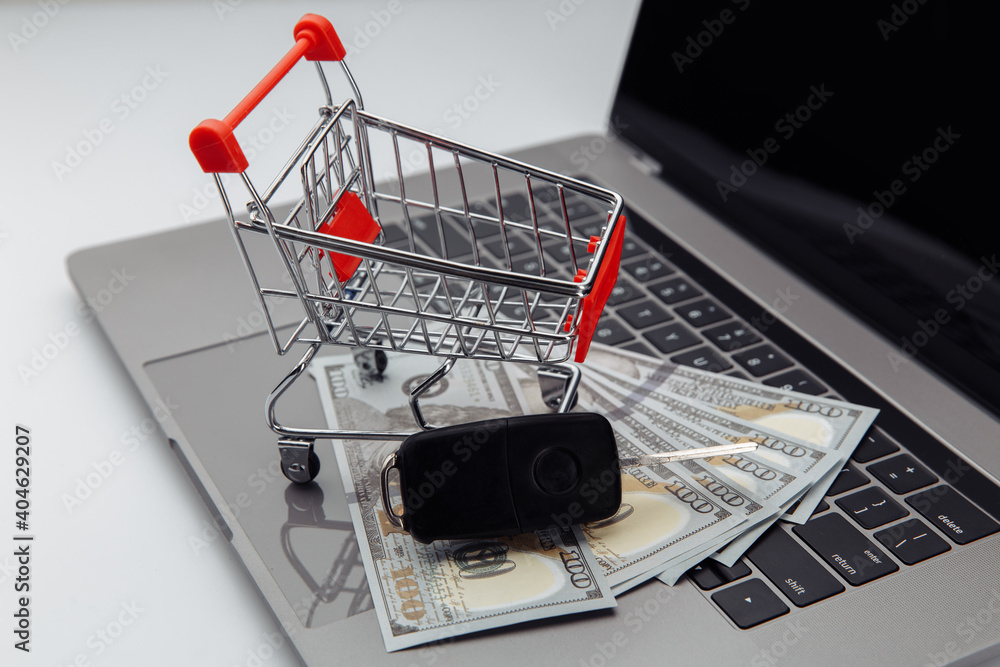 Car keys with dollar banknotes and shopping cart on keyboard. Online purchase car concept.