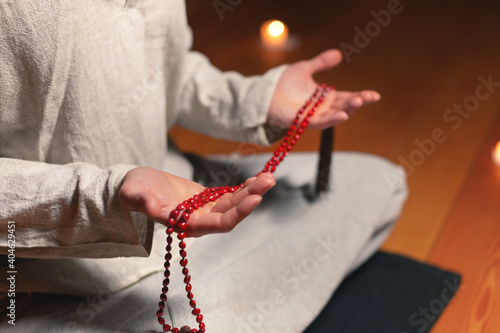 close-up the male hand of a monk practicing meditation holds a red rosary in a dark room by candlelight. Practice and enlightenment
