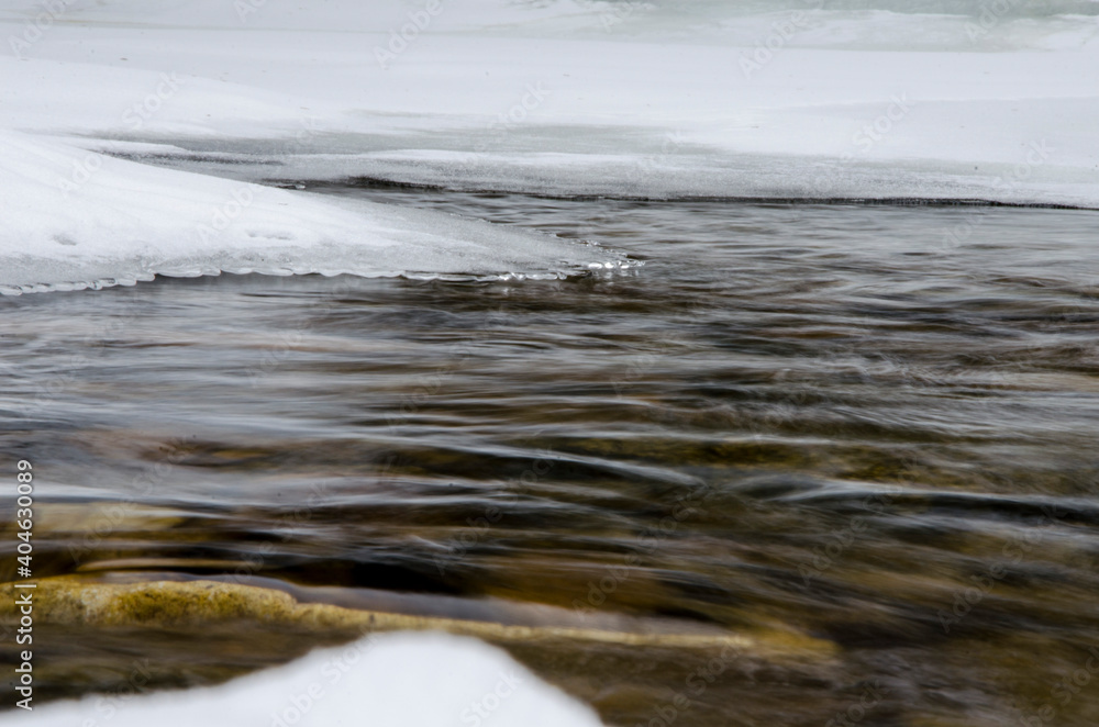 The frozen river, the water was covered with ice, white snow fell. Winter view, cold day.