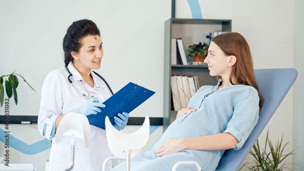 Happy Pregnant Woman Visit Gynecologist Doctor at the Medical Clinic. Female Doctor Examine Pregnant Young Mother to Check Up Her Healthcare. Teenage Pregnancy. Consulting of Pregnant at Clinic. Happy Pregnant Woman Visit Gynecologist Doctor at the Medical Clinic. Female Doctor Examine Pregnant Young Mother to Check Up Her Healthcare. Teenage Pregnancy. Consulting of Pregnant at Clinic.