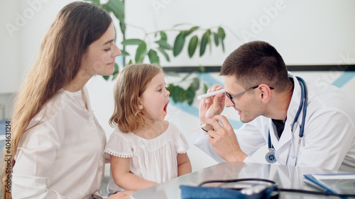 Male Doctor Pediatrician Examining an Ill Sad Kid Girl at Medical Visit With Mother in the Hospital. Male Family Doctor Examining and Consulting to Mother and Her Ill Child.