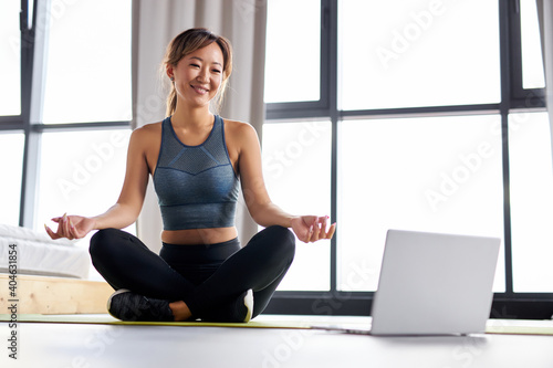 woman enjoying yoga on mat alone at home, giving online educational yoga workshop, using laptop. strong female in sportswear