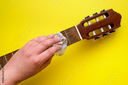 the hand holds a rag and wipes the neck of a guitar without strings