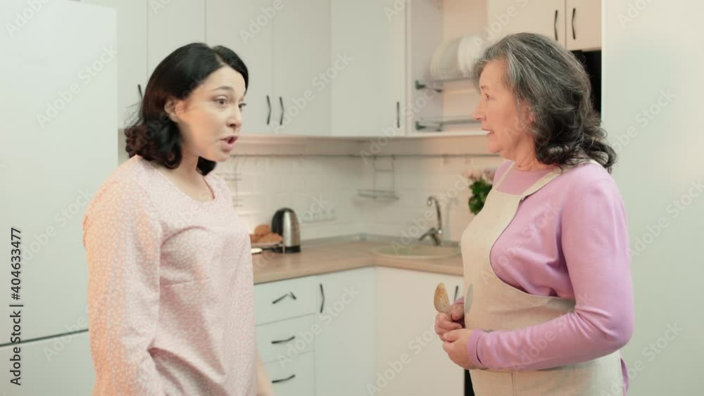 Aged mother in apron arguing with daughter in kitchen, generation gap, conflict Aged mother in apron arguing with daughter in kitchen, generation gap, conflict