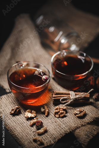Food photography. Cinnamon tied with twine on burlap. A glass cup of hot tea on a dark wooden background.