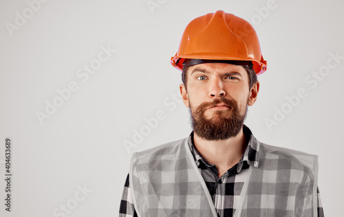 the architect gestures with his hands in an orange hard hat on a light background and a reflective vest