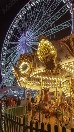Golden kids carousel with animals in front of a big wheel at night on a fun fair in Hyde Park, London. 