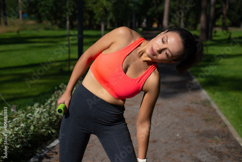 Sporty young woman stretching after exercising on a running way in the beautiful park. Workout outdoor concept.