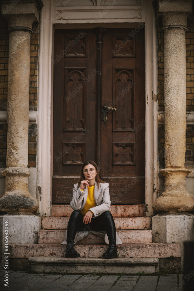 Influencer sitting on the stairs of an old building and posing with hand on her chin.
