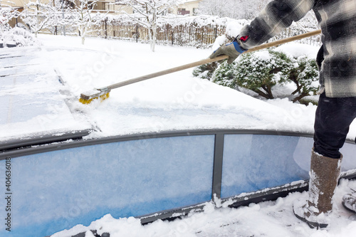 A man cleans snow from a water pool outdoor. Water pool care in winter.