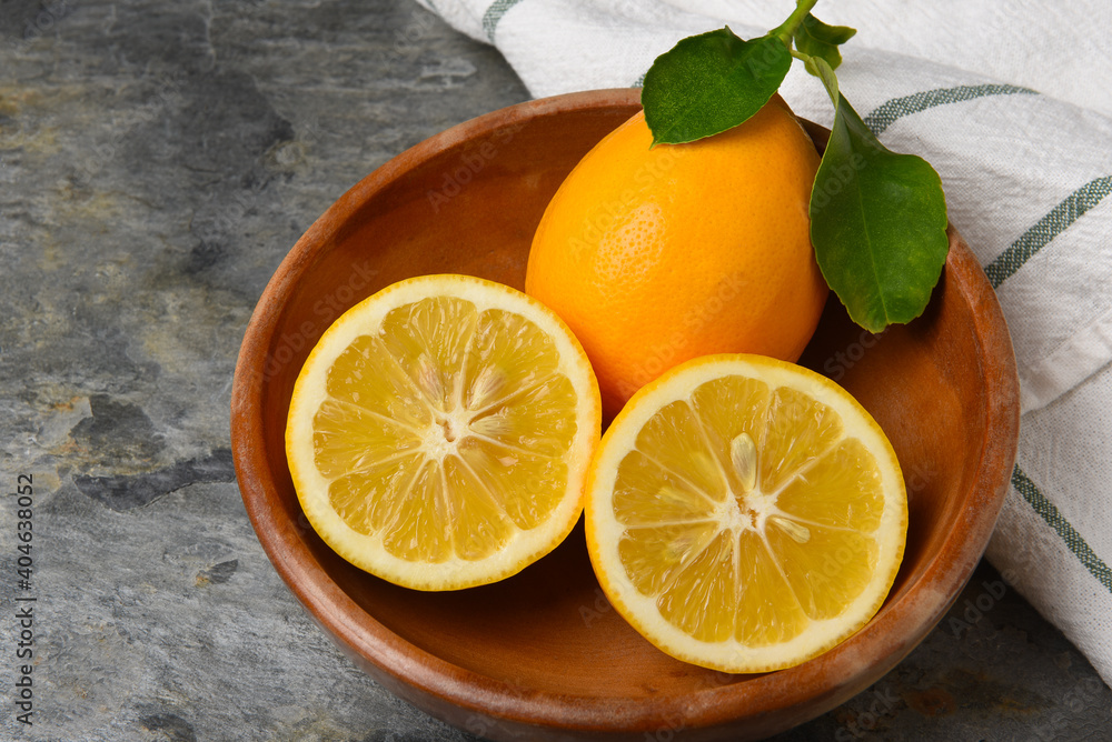 Closeup of a cut lemon and whole fruit with leaves in a wooden bowl on gray slate. Closeup of a cut lemon and whole fruit with leaves in a wooden bowl on gray slate.
