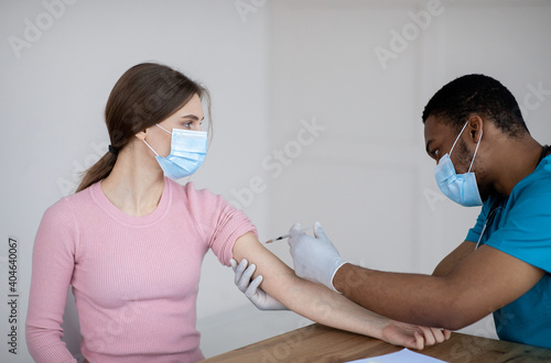 Black doctor making covid-19 vaccine injection to female patient at clinic. Medical treatment against global pandemic
