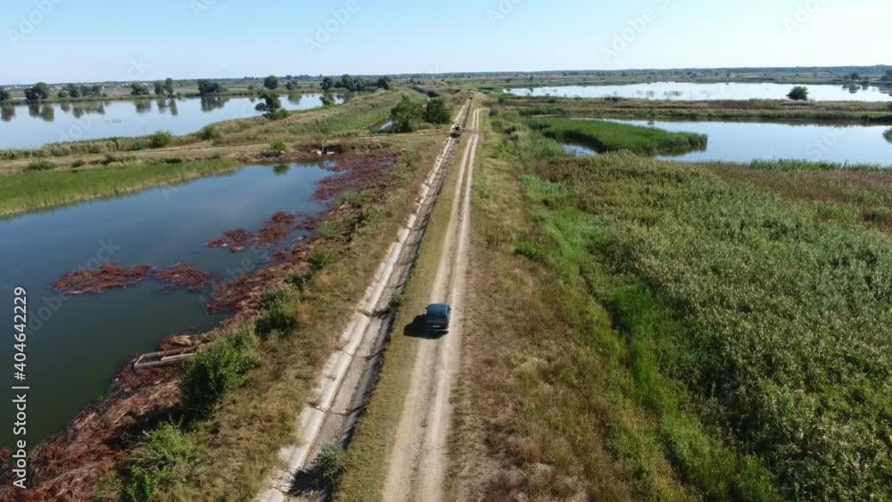 Aerial shot of a moving car on a soil dam road of a fishing plant in summer Aerial shot of a moving car on a soil dam road of a fishing plant in summer