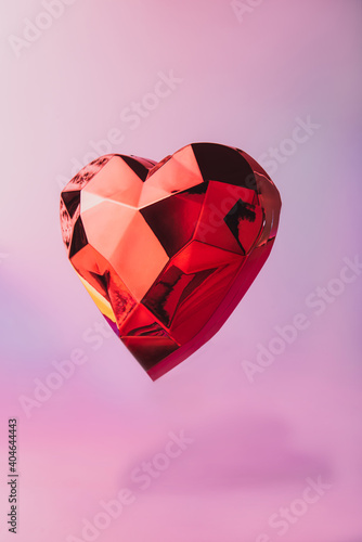 Sparkling levitating geometric heart with shadow on a neon pink background. Red polygonal heart for Valentine s day card. Love concept. Festive vertical background with copy space. Minimalism style.