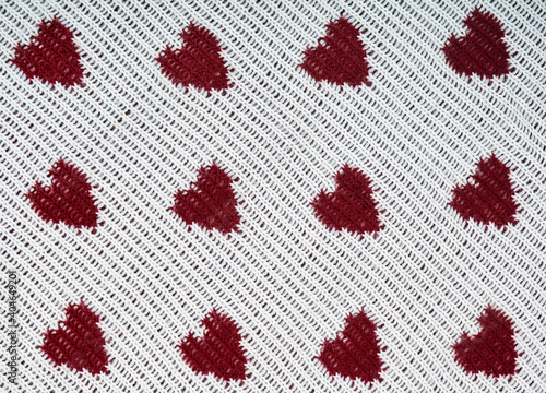 Knitted white background with a red pattern in the shape of heart.