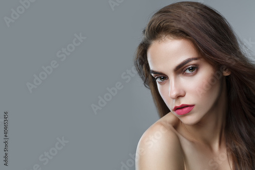 Fashion studio portrait of a beautiful young girl with an evening make-up and hairstyle on a gray background.
