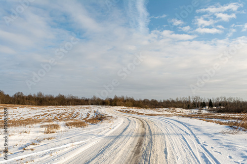 The winding snow-covered road goes into the horizon. Sunny winter day with blue skies and small clouds