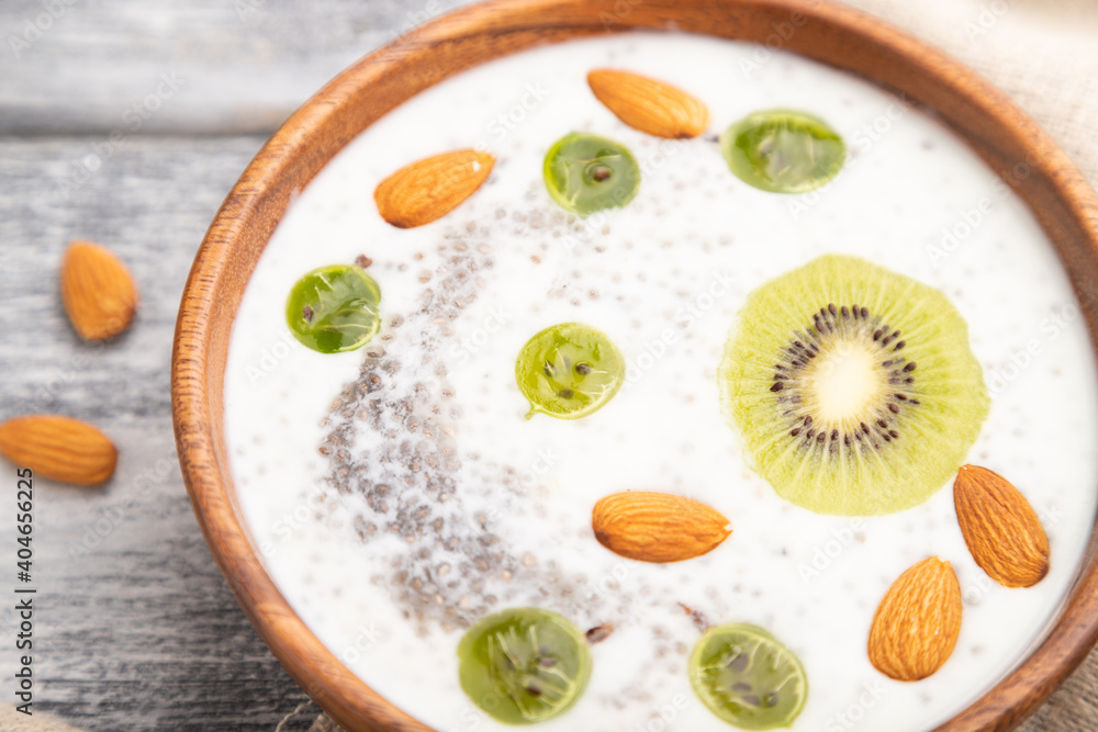 Yogurt with kiwi, gooseberry, chia and almonds in wooden bowl on gray wooden background. Side view, close up, selective focus. Yogurt with kiwi, gooseberry, chia and almonds in wooden bowl on gray wooden background. Side view, close up, selective focus.