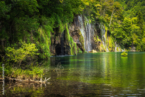 Fototapeta Naklejka Na Ścianę i Meble -  Beautiful waterfall illuminated by sunlight with reflections in lake. Green lush forest, Plitvice Lakes National Park UNESCO World Heritage in Croatia