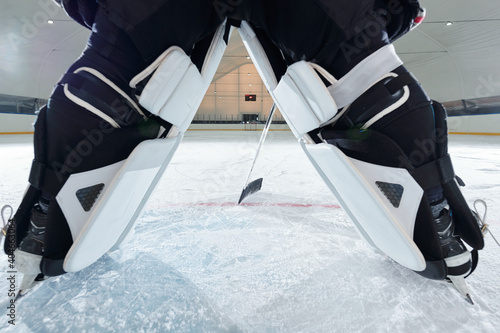 Photography Back view of legs of hockey player in skates standing on rink and holding stick