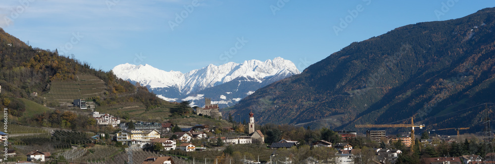 Picturesque mountain landscape in Naturns in South Tyrol in autumn, in the fore an old church, castle and old buildings and in the background the snow-covered Alps, no people