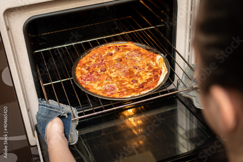 Woman hands taking out ready pizza out of the oven. Cooking at home. Low DOF.