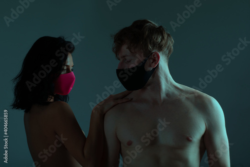 Coronavirus Concept. Portrait of young caucasian couple in protective medical masks standing over light background in studio. 