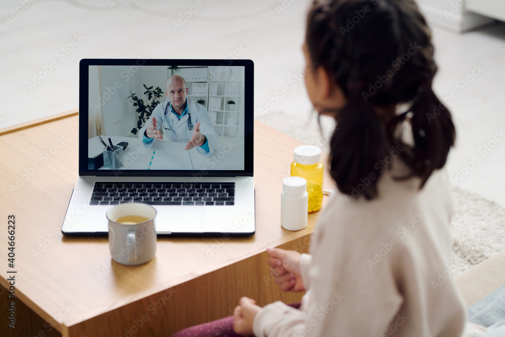 Mature doctor on laptop display giving medical recommendations to little girl Mature doctor on laptop display giving medical recommendations to little girl
