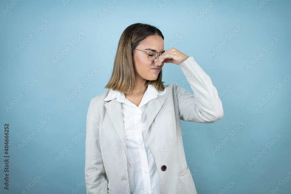 Young business woman over isolated blue background smelling something stinky and disgusting, intolerable smell, holding breath with fingers on nose Young business woman over isolated blue background smelling something stinky and disgusting, intolerable smell, holding breath with fingers on nose